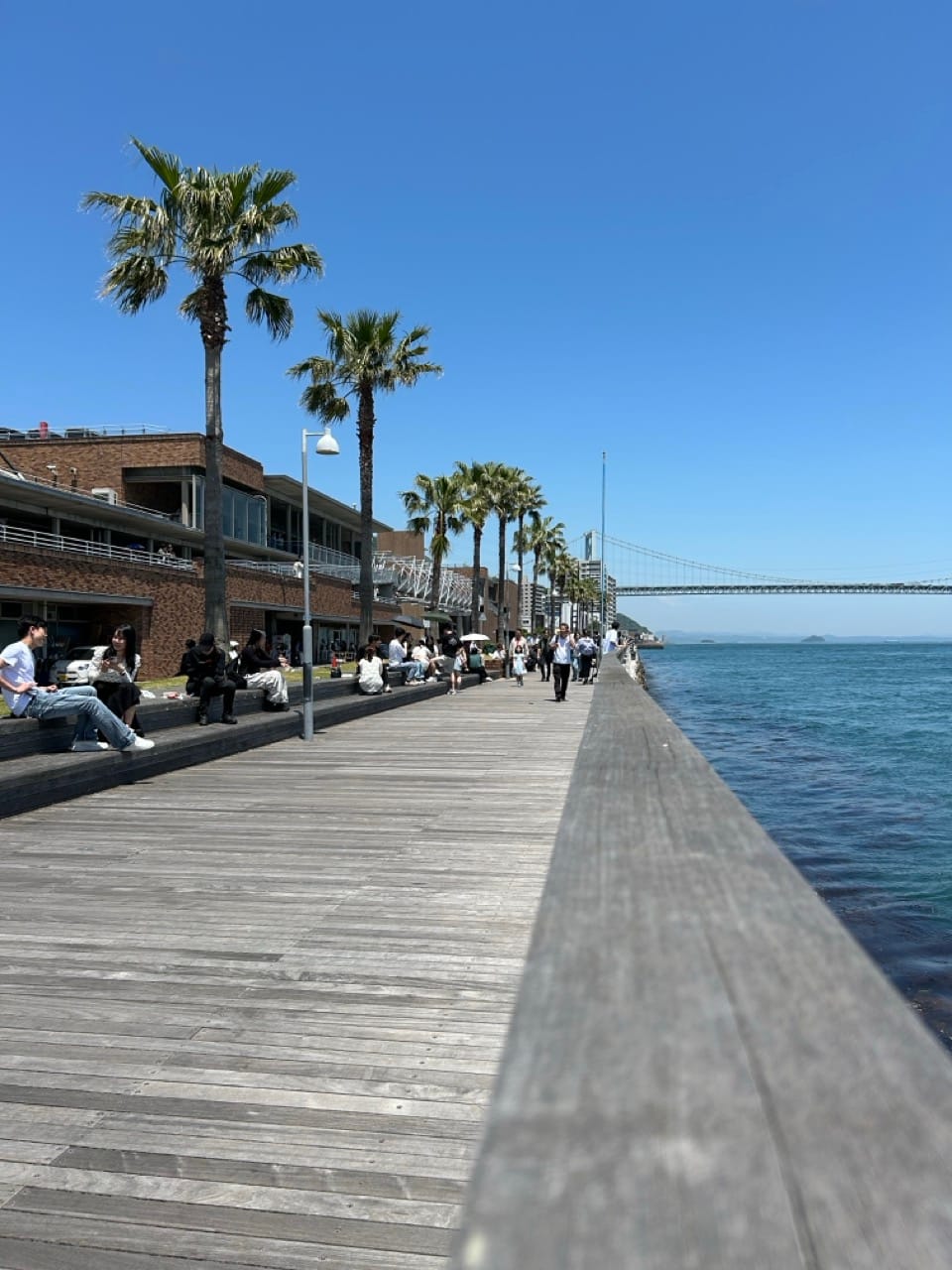 People enjoying their lunches sitting in the sun along the boardwalk.