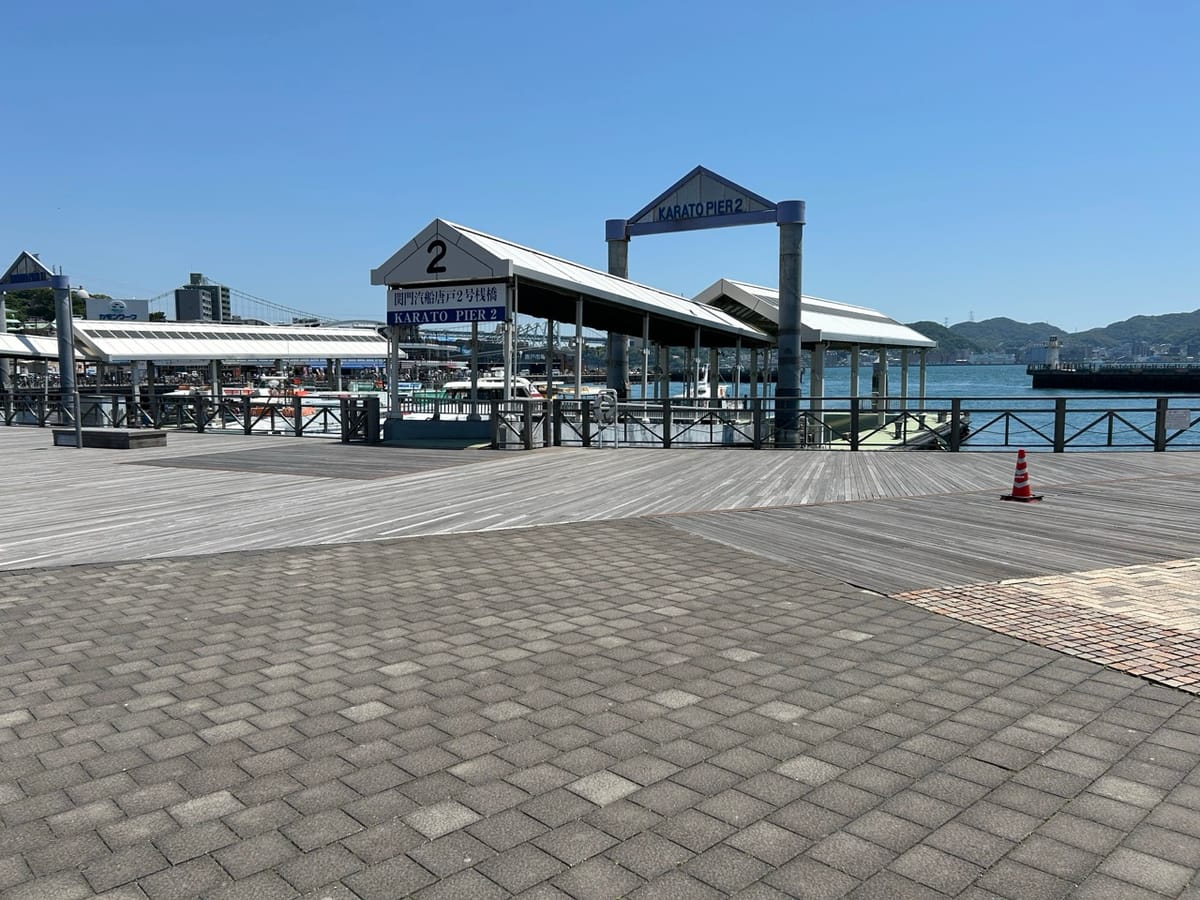 Piers with concrete tiles and wooden planks on the floor in the foreground and the sea and mountains in the background.